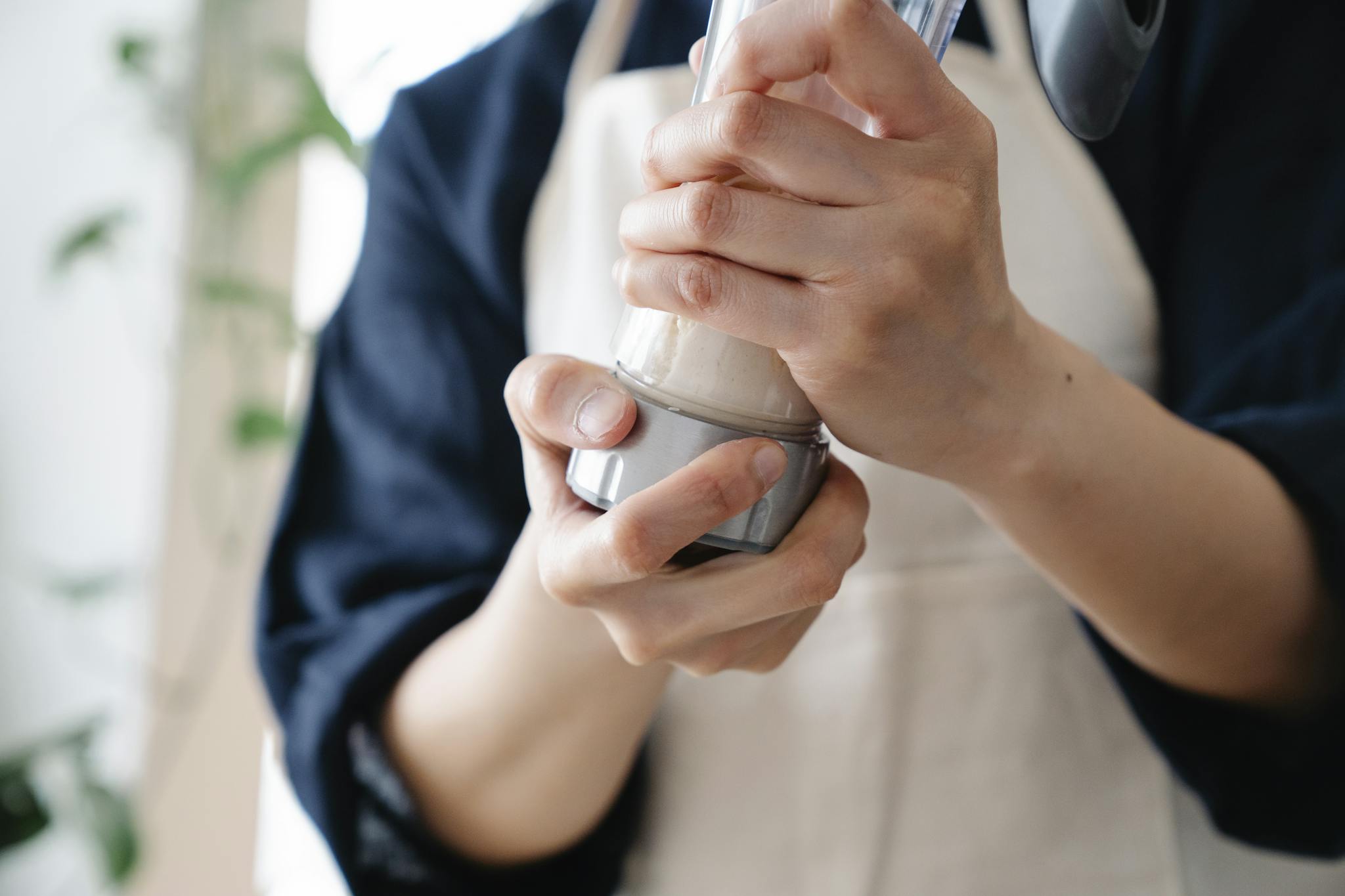 A person wearing an apron holds and shakes a protein shaker indoors. Casual food preparation scene.