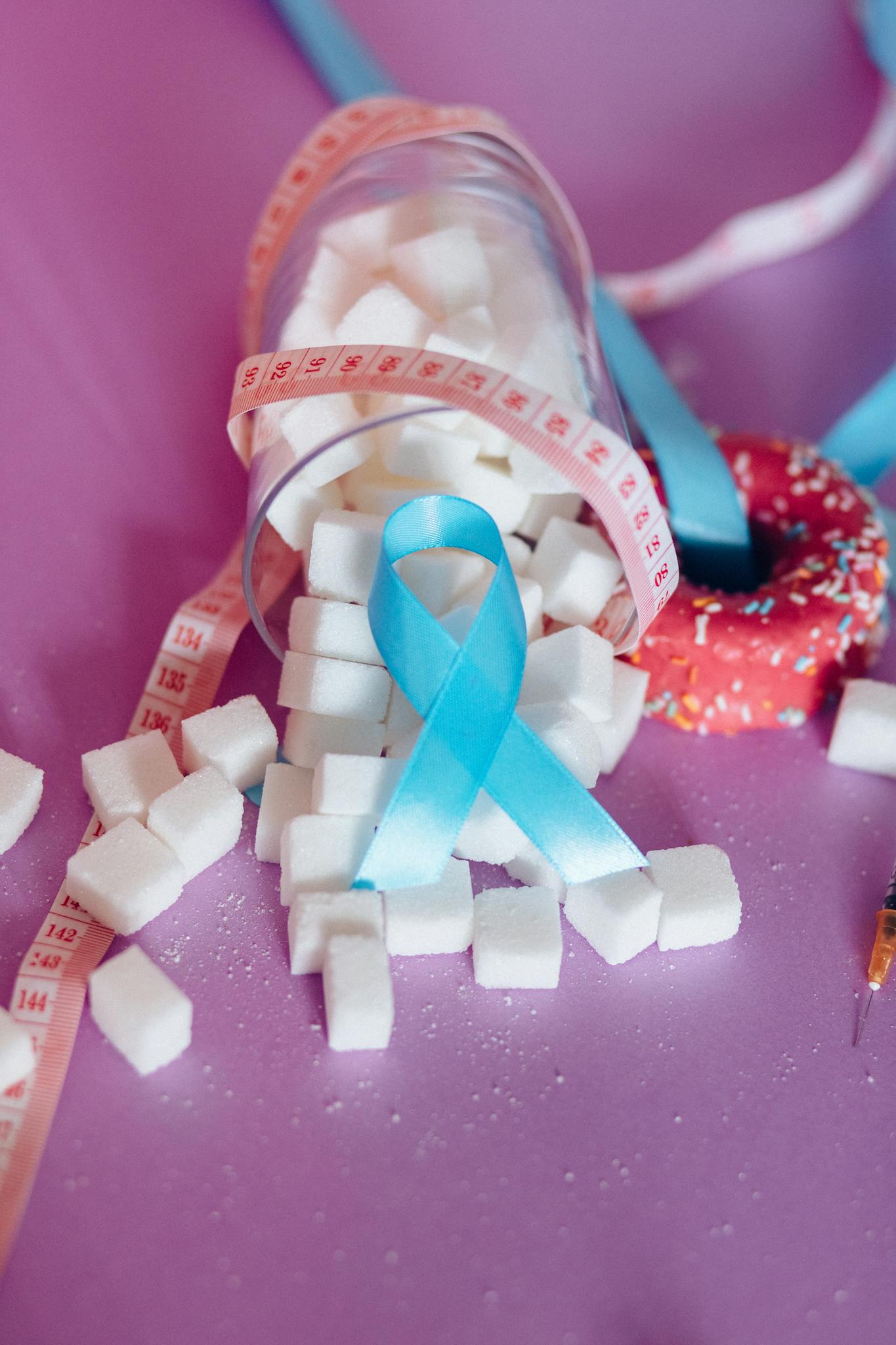 Image highlighting diabetes awareness with sugar cubes, blue ribbon, and measuring tape on purple background.