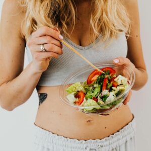Woman in sports attire enjoys a fresh, nutritious salad, embodying a healthy lifestyle.