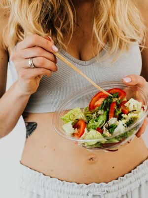 Woman in sports attire enjoys a fresh, nutritious salad, embodying a healthy lifestyle.