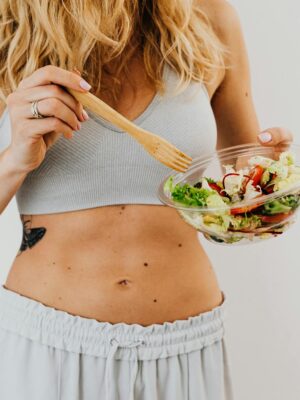 Young woman in sports attire holding a fresh salad bowl, promoting a healthy lifestyle.