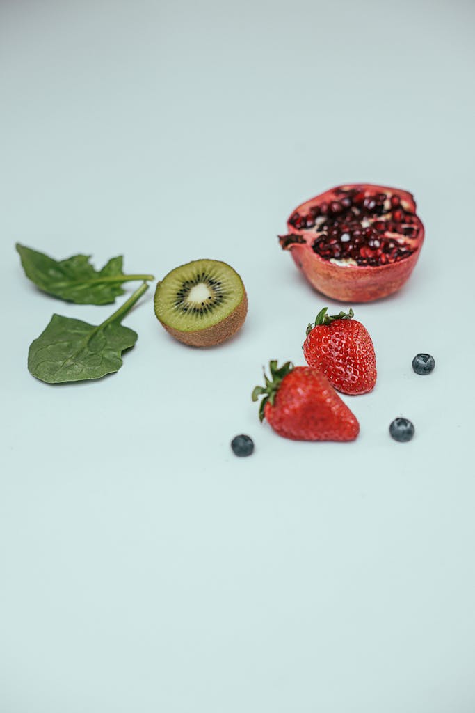 A vibrant mix of strawberries, kiwi, pomegranate, blueberries, and spinach leaves on a white background.