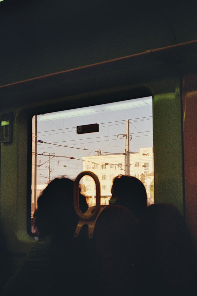 Silhouette view of passengers on a train looking out to an urban landscape through a window.